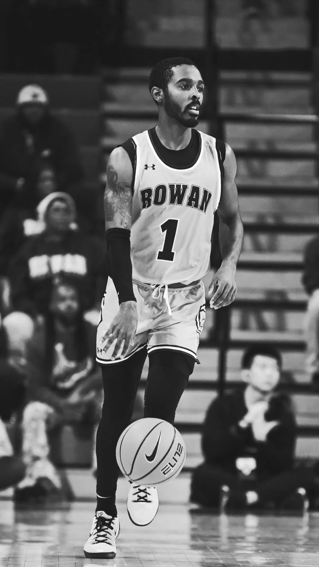 Black-and-white image of Fareed Burton Jr. dribbling in a white Rowan College number one jersey